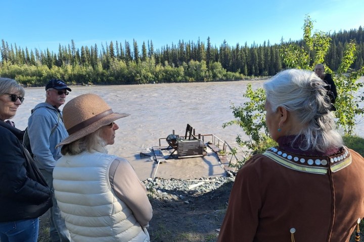 Four people standing by a river, looking at a small platform with equipment.