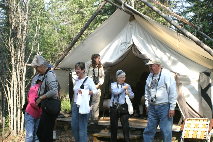 Group of people standing outside a canvas tent in a forest.