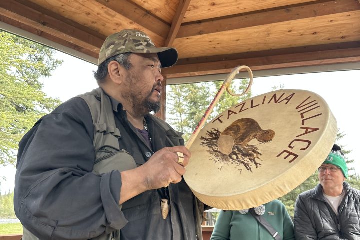 Person playing a traditional drum under a wooden pavilion.